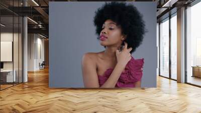 Amazing black young woman with afro hairstyle using a lovely women's perfume on grey background. Portrait of sexy female black model in dress trying a fragrance indoors. Wall mural