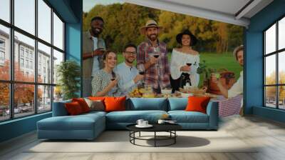 Beautiful happy friends toasting with red wine smiling enjoying summer celebratory picnic in the vineyard. Social gathering. Wall mural