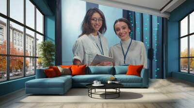 Couple of smart women IT technicians checking open rack server cabinet checking updating hardware cooperating in futuristic digital room of data center. Wall mural