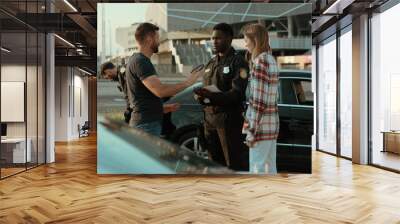 People talking with the police in road accident area. Young offended woman argue with the driver after car crash. Focus on afro american baffled policeman near the car. Accident on the city road. Wall mural