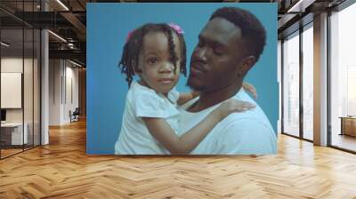 Portrait of cheerful african american dad holding and hugging cute little daughter isolated on blue background. Wall mural