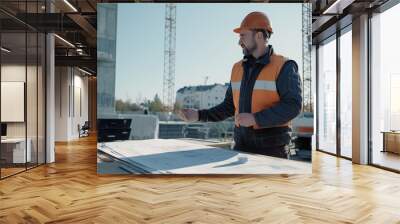 Construction worker in a hard hat and safety vest discussing blueprints at a building site Wall mural