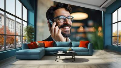 Smiling happy young bearded Latin business man executive or employee wearing eyeglasses holding cell phone making mobile call at work on cellphone standing in modern office. Close up, Generative AI  Wall mural