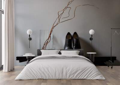 Black men's shoes with lacing on the table leaning on the wall, next to it is a vase with a dry branch Wall mural