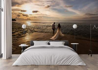 Bride and groom go to sea on the beach at sunset Wall mural