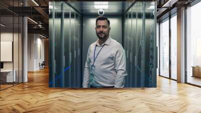 Adult IT worker in white shirt standing among server racks in data center smiling at camera Wall mural