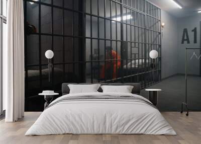 African American inmates in detention center or correctional facility. Depressed man in orange uniform sits on prison bed and looks at barred window. Prisoners serve imprisonment term in jail cell. Wall mural