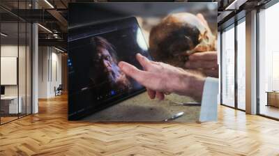 Archaeological lab: Two researchers or scientists examine fossil skull under lamp, discuss 3D model and visualization of prehistoric extinct human head displayed on digital tablet computer screen. Wall mural