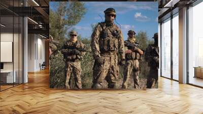 Group of soldiers in a camouflage and the hidden persons with weapon pose and look in the camera Wall mural