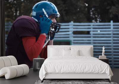 Side view of bearded American football player putting on jaw protector and helmet before game Wall mural