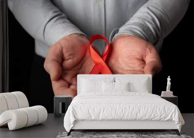 A man showing his two open hands holding a red ribbon in support of World AIDS Day. Understanding and empathy for hiv patients Wall mural