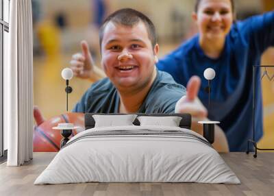 Two happy young individuals, one with down syndrome, giving a thumbs up and smiling on a basketball court Wall mural