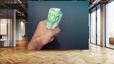 Male hand grabbing money rolled up, hundred euro bills, blue light coming from top right corner Wall mural