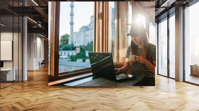 A young female tourist blogger freelancer working on a laptop in a cafe in Istanbul. A view from the window to the world-famous Blue Mosque also called Sultanahmet. Wall mural