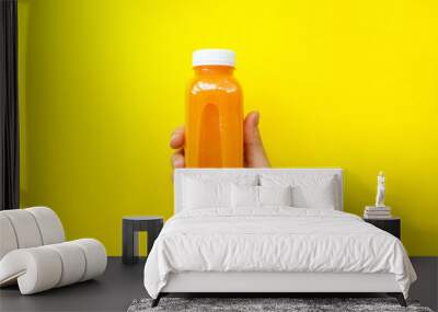 Female hand holding plastic bottles with orange juice or smoothie on yellow background. The concept of diets, detox. Bright background, flat lay, top view Wall mural