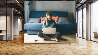 Girl working on laptop from home or student studying from home or freelancer. She is watching an online course or doing homework or surfing the net. Wall mural