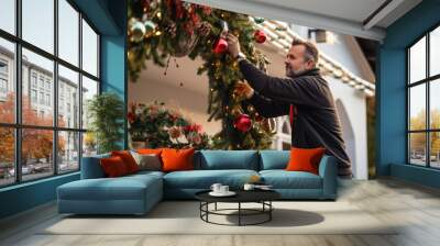 A man preparing setting up the Christmas decorations and fairy lights in his front yard before the holiday season is starting Wall mural