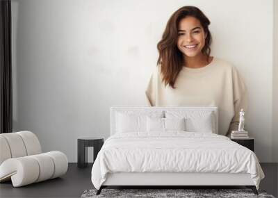   beautiful woman wearing a plain tan sweatshirt standing in front  white wall with modern decor in the background in a happy mood Wall mural