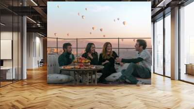 Four friends or two couples have fun whilst having breakfast outdoor with fruits, breads and drinks with a beautiful view to the balloons in Cappadocia, Turkey  Wall mural