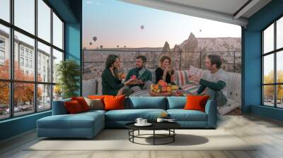 Four friends or two couples have fun whilst having breakfast outdoor with fruits, breads and drinks with a beautiful view to the balloons in Cappadocia, Turkey  Wall mural