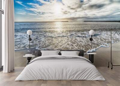 Beautiful shot of the ocean water arriving the shore and the cloudy sky in the background Wall mural