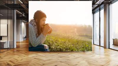 Asian lifestyle women wearing sweater, sitting and drinking hot coffee or tea relax outdoor in the sunrise morning sunny day at tea plantation nature Wall mural