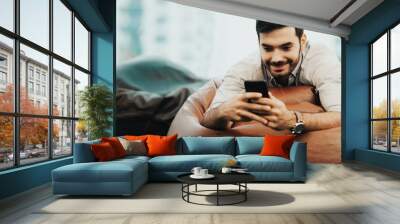 Smiling businessman using and relax smartphone device while sitting on sofa at home.  Man cheerful hipster guy typing an sms message at social network.  Technology Concept. Wall mural