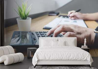 Businessman working on a graph document financial report and analysis calculation investment cost with calculator at office desk and other objects around Wall mural