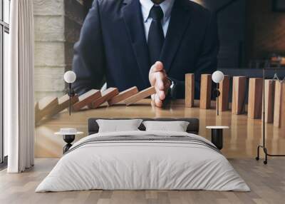 close up of businessman hand stopping falling wooden dominoes effect from continuous toppled or risk Wall mural