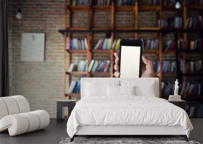 Man holding blank screen of a smartphone at the library. Wall mural