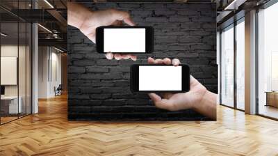 Two hands holding horizontal the black smartphone with blank screen, old brick wall background. Wall mural