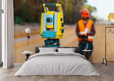 Surveyor engineer with equipment (theodolite or total positioning station) on the construction site of the road or building with construction machinery background Wall mural