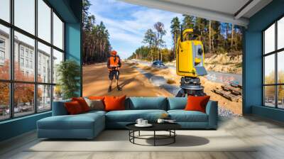 Surveyor engineer with equipment (theodolite or total positioning station) on the construction site of the road or building with construction machinery background Wall mural