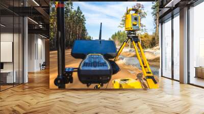 Surveyors equipment (theodolite or total positioning station) on the construction site of the road or building with construction machinery background Wall mural