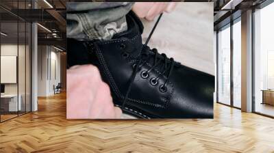 Man in a military uniform ties the laces on his black shoes. Wall mural