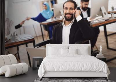 Disabled arab man in wheelchair working in office. Man is working on laptop. Wall mural