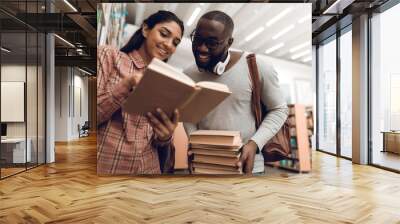 Ethnic indian mixed race girl and black guy in library. Students are looking for books. Wall mural