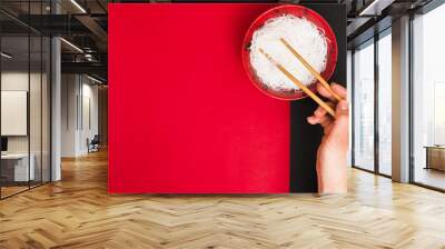 Person's hand uses chopsticks to pickup tasty steamed noodles in bowl over dual table Wall mural