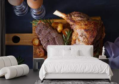 Roast leg of lamb with potatoes and rosemary on serving wooden board. View from above, top view Wall mural