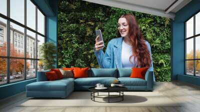 Beautiful young business woman smiling while looking at her smart phone. close-up of hands of a girl who writes a message in a mobile phone, empty space for text Wall mural