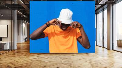 Black ethnic man dancing covering his face from the sunlight with hat Wall mural