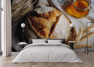 Top view of sourdough bread with a crackling crust, displayed on a linen cloth, surrounded by wheat stalks and a small jar of honey. Wall mural