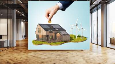 A hand puts a coin in a house with solar panels and windmills Wall mural