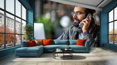 Focused young businessman talking on a landline phone while working on a computer in a busy office. Wall mural