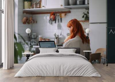 Back view of young woman with ginger hair afro style on kitchen working with laptop, AI generative Wall mural