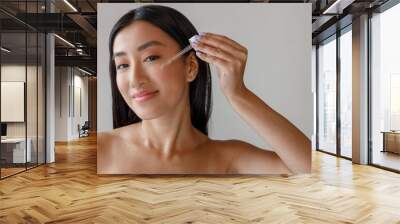 Asian young woman applying vitamin serum on her face Wall mural