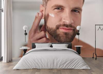 Attractive mature man applies cream onto skin under eye in bathroom Wall mural