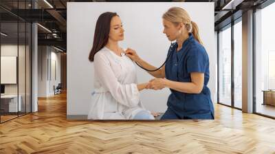 Caring female doctor use stethoscope examine patient heart rate at consultation in hospital Wall mural