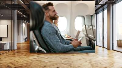 Cheerful bearded man using smartphone in airplane Wall mural