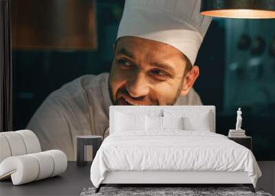 Close up of smiling male chef in uniform standing on kitchen of restaurant and looking away Wall mural